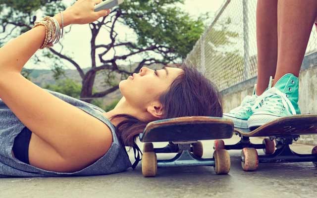 girl lying down on skateboard looking at her phone